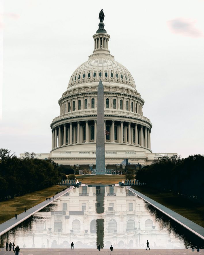 Old stone government building exterior with statue on top near pond between trees in USA